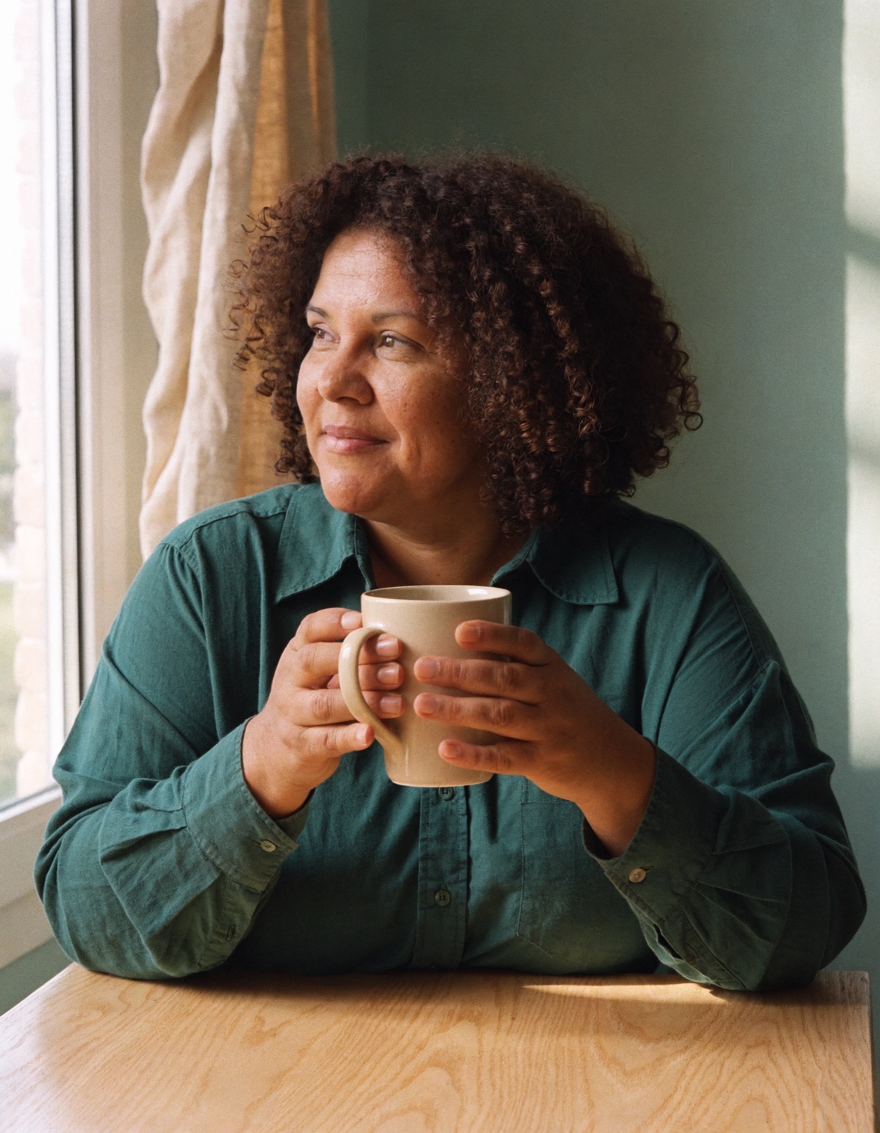 Woman sitting by a window, holding a mug.